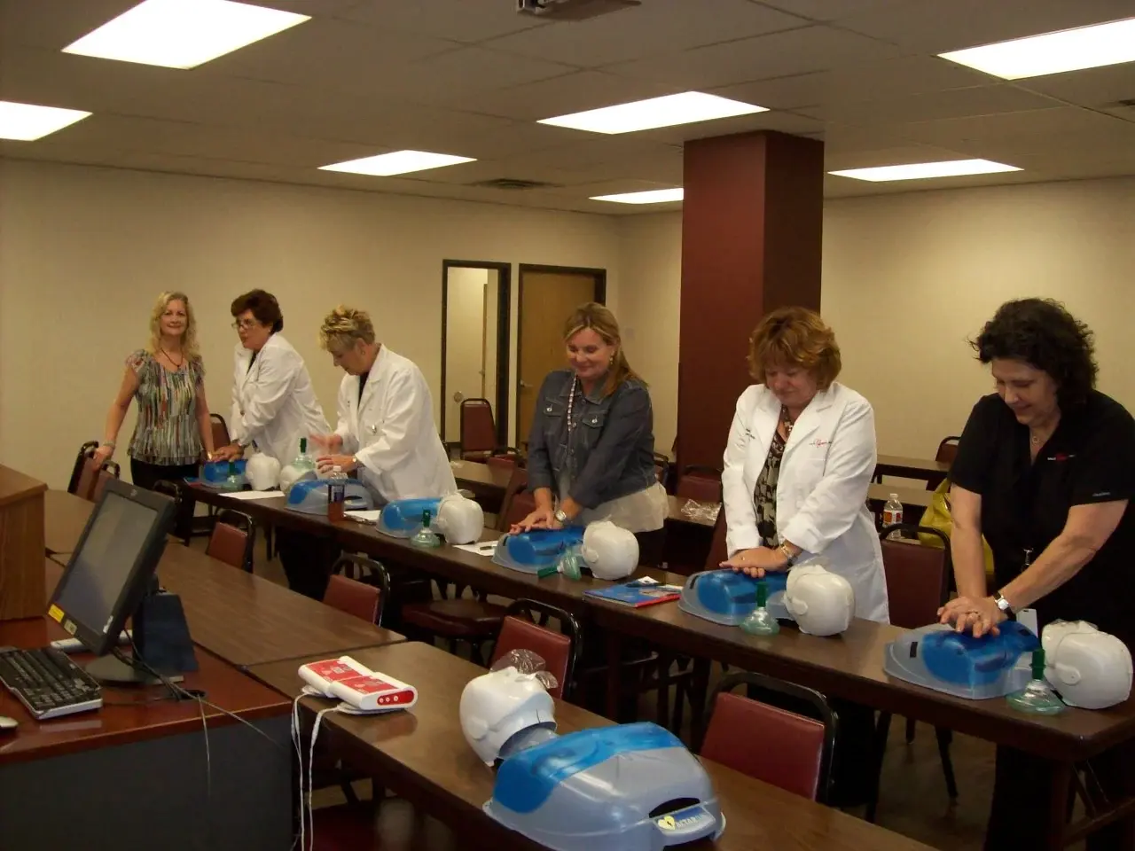 Healthcare staff in white coats practising chest compressions on training manikins in a Texas Heart CPR class.
