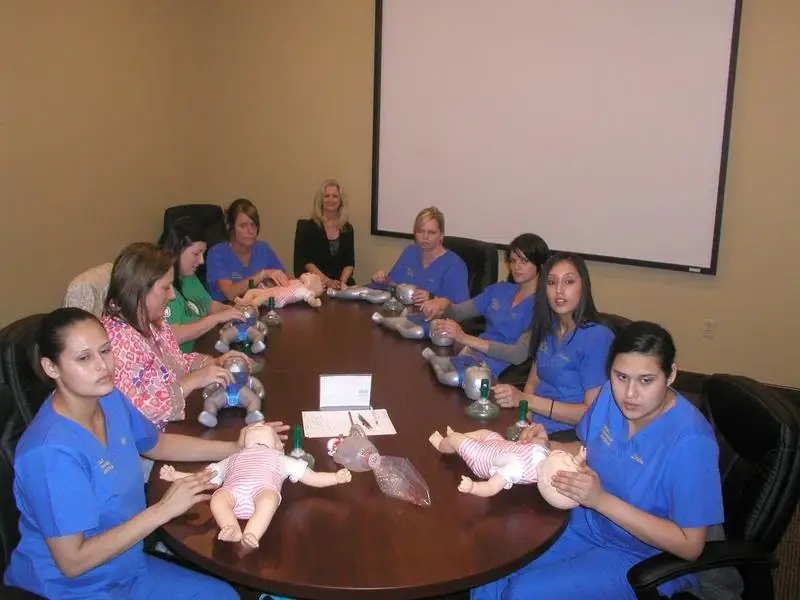 A staff class seated around a conference table practising infant CPR with manikins and barrier masks.