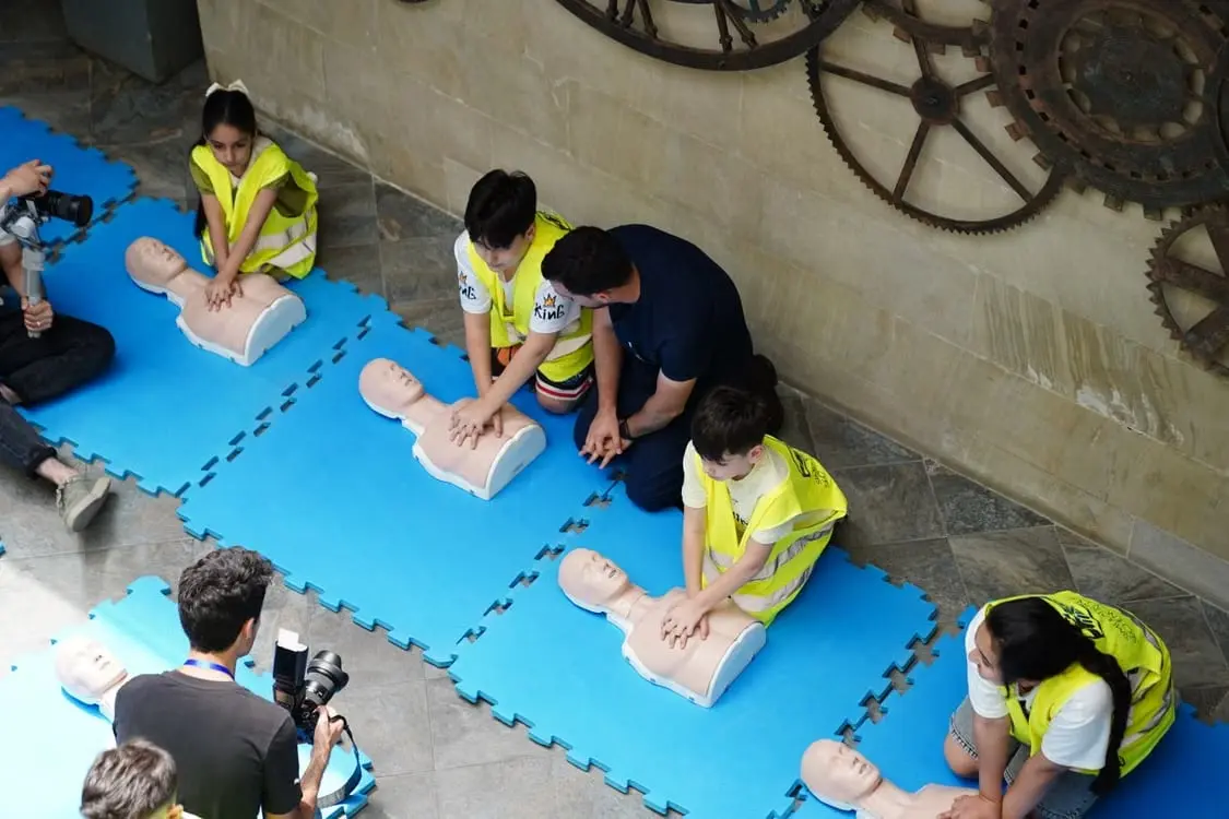 An instructor coaching a row of students practising compressions on training manikins.